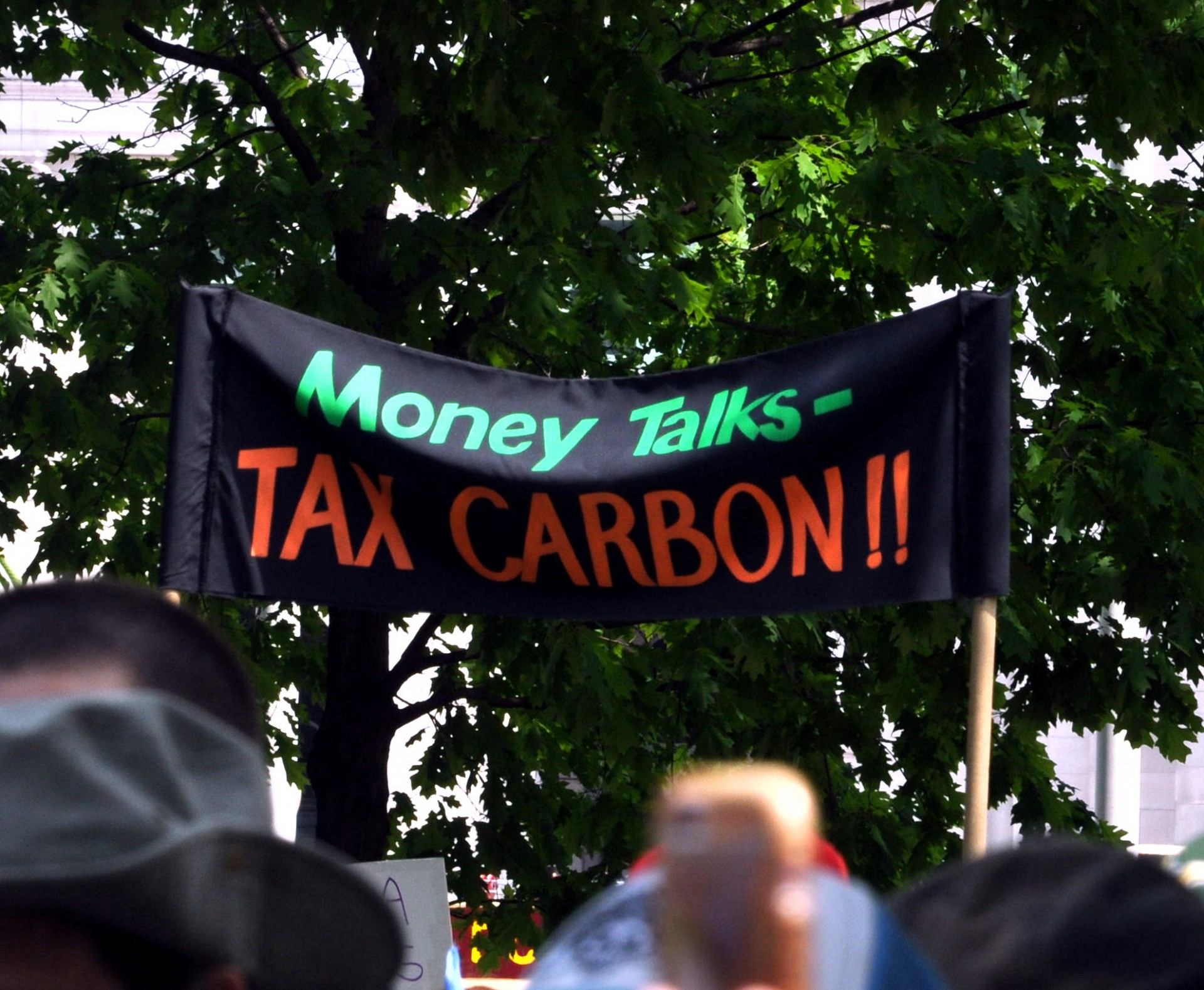 A black banner is held above a crowd that reads: Money Talks - TAX CARBON