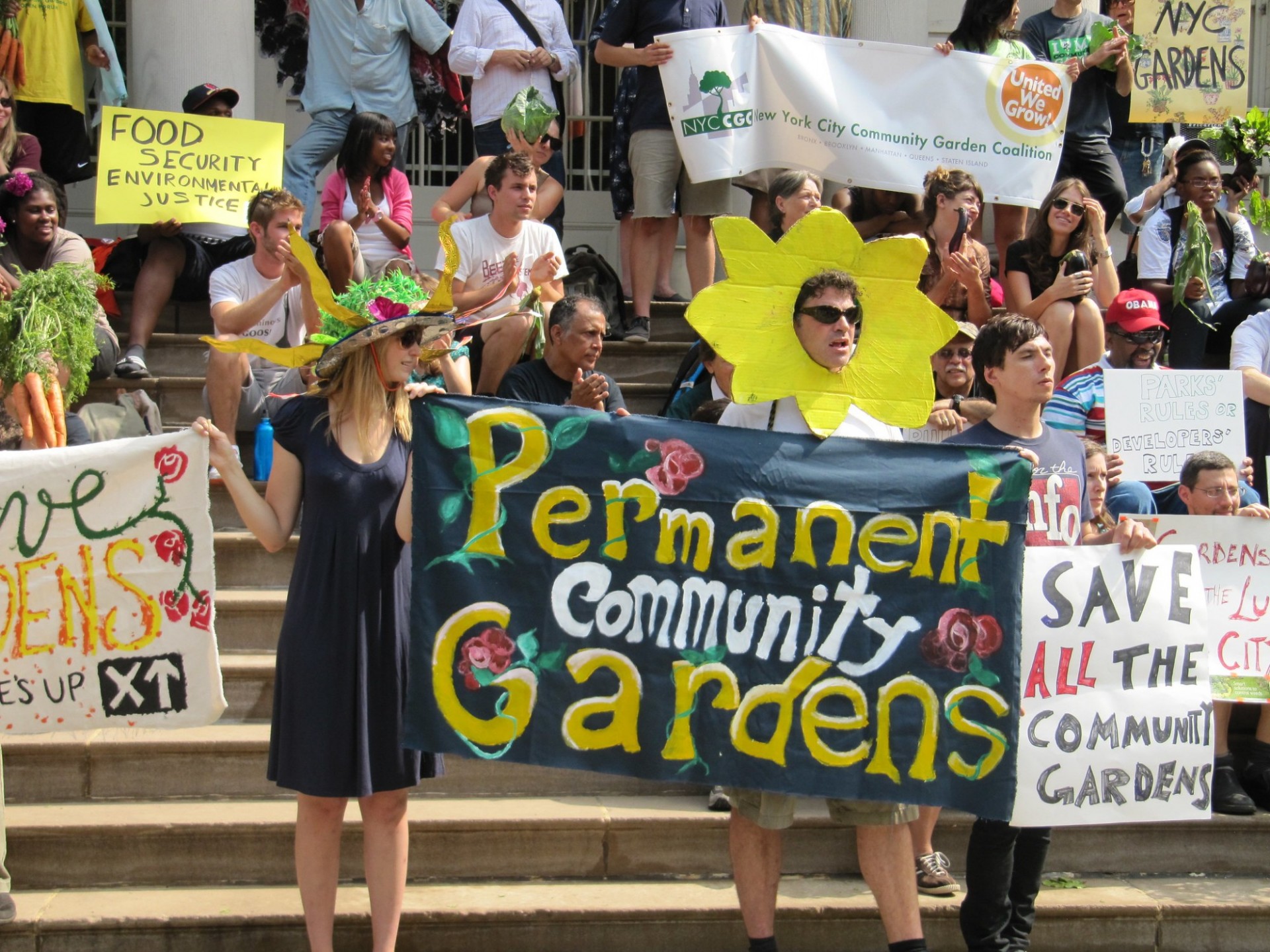 Community gardeners on the steps of a building holding signs in support of community gardening