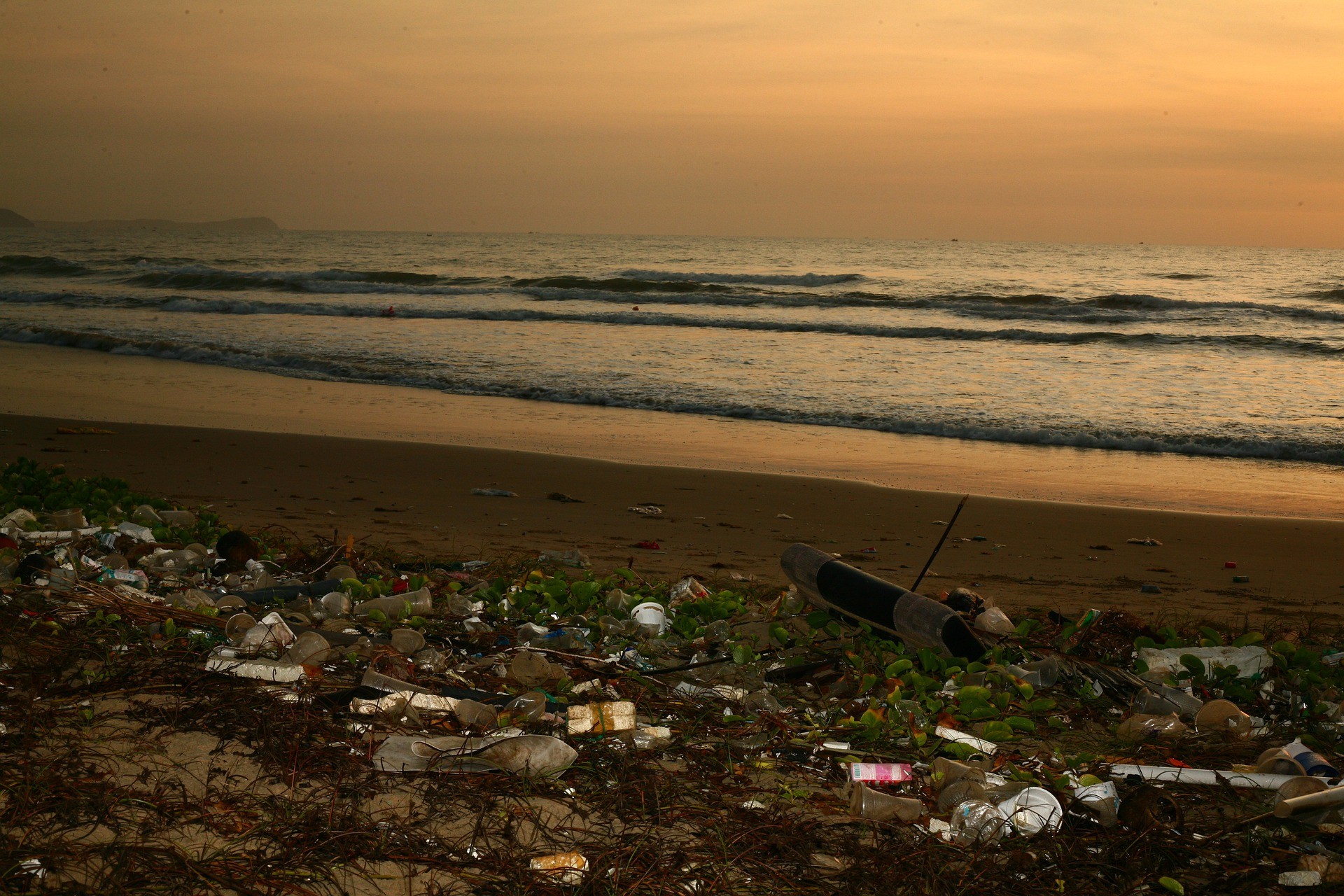 Trash on a beach at sunset with waves in the distance.