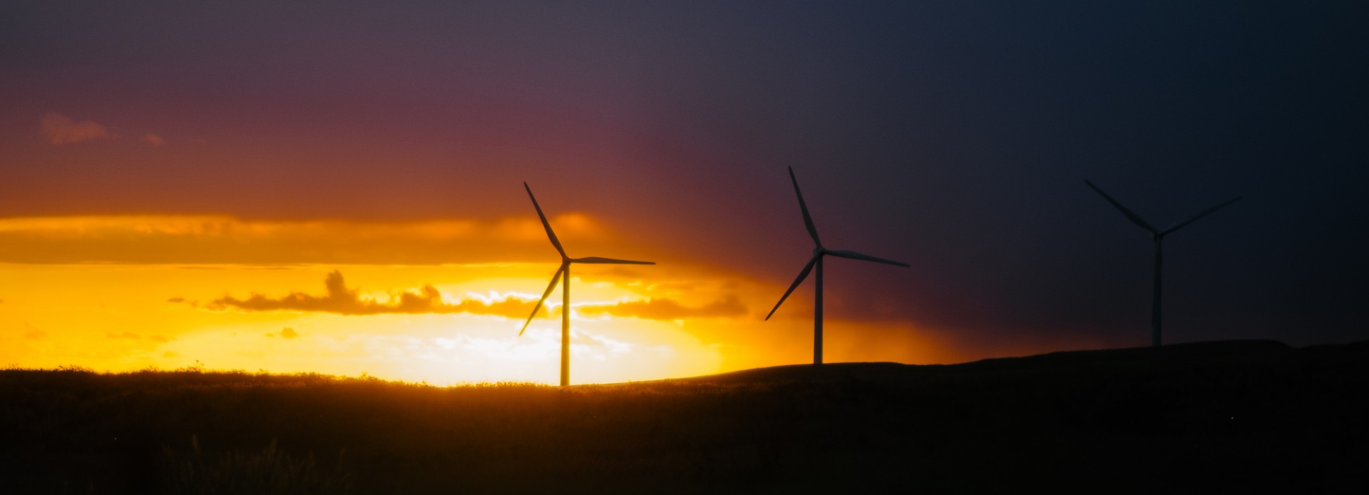 Windmills on a hilly horizon with the sun setting behind them.